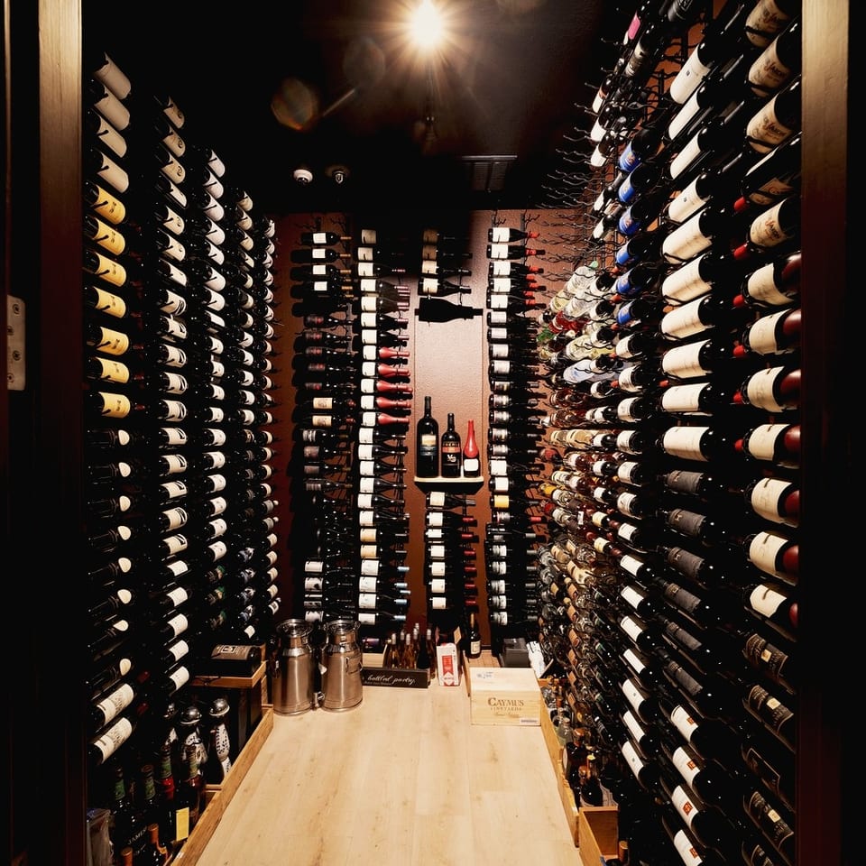 Narrow, warmly lit wine cellar lined with hundreds of bottles and featuring a wooden tasting table.